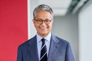 Salim Ramji in a business suit, smiling in a modern office setting.
